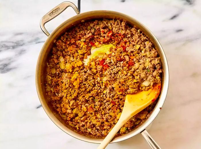 A pan of seasoned ground beef and onions being stirred with a wooden spoon