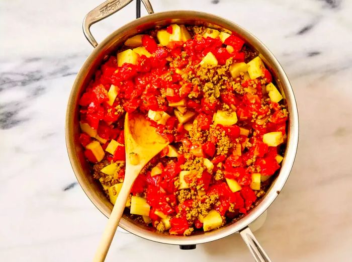 A skillet of cooked ground beef mixed with chopped tomatoes and potatoes