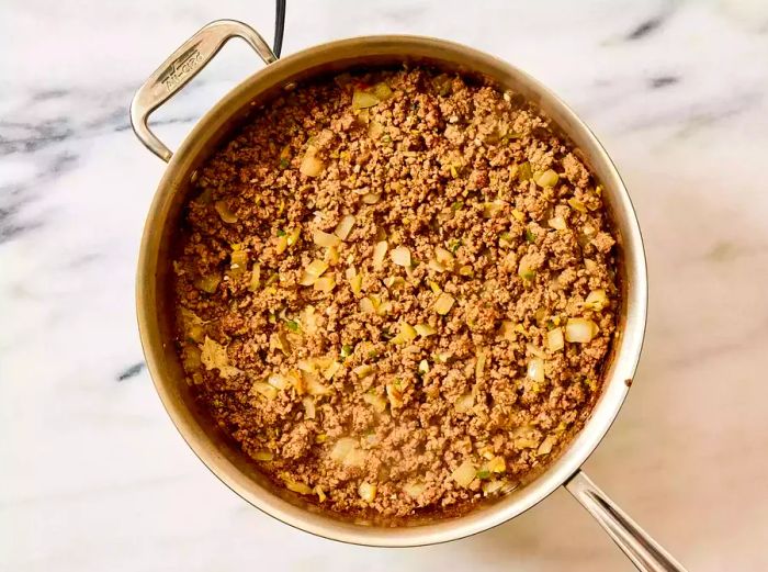 A large skillet with browned ground beef, seasoned with spices, and chopped onion