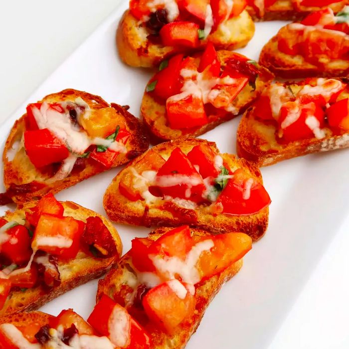 A close-up of Tomato Bruschetta served on toast, presented on a white platter