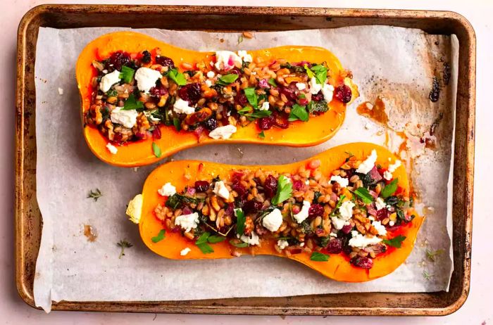 Stuffed and baked butternut squash on a parchment-lined baking sheet, topped with goat cheese.