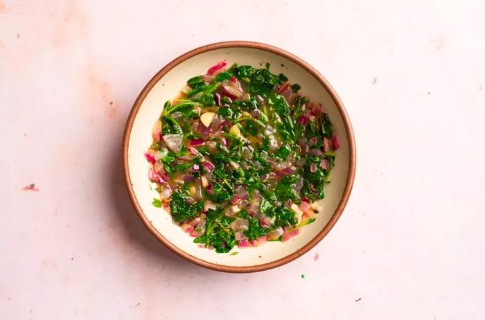 A bowl of chopped kale mixed with onions and seasonings.