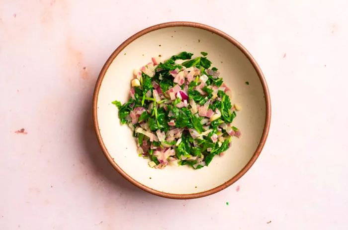 A bowl of sautéed onions and chopped kale.