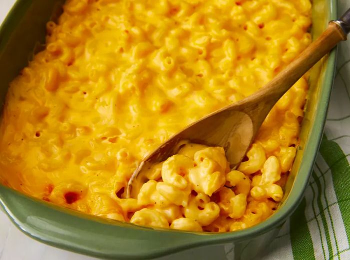 A top-down view of a green casserole dish filled with mac and cheese, with a spoonful resting inside.