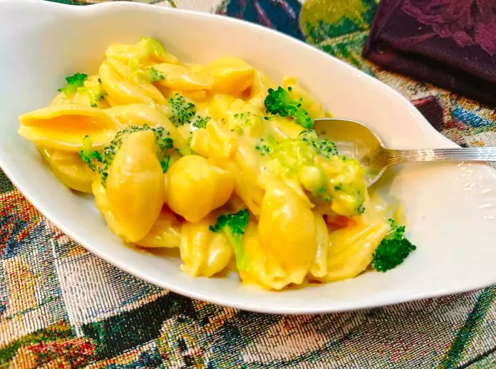 A bowl of oval-shaped pasta shells smothered in cheese sauce and topped with broccoli.