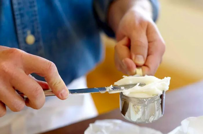 A person leveling off lard in a measuring cup