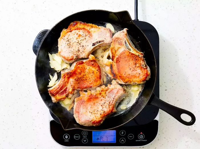 Aromatics sizzling in a cast iron skillet alongside golden-brown pork chops.