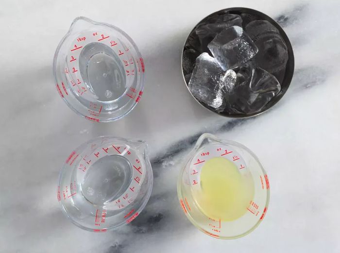 Overhead shot of a shaker filled with ice and three measuring cups containing various margarita ingredients.