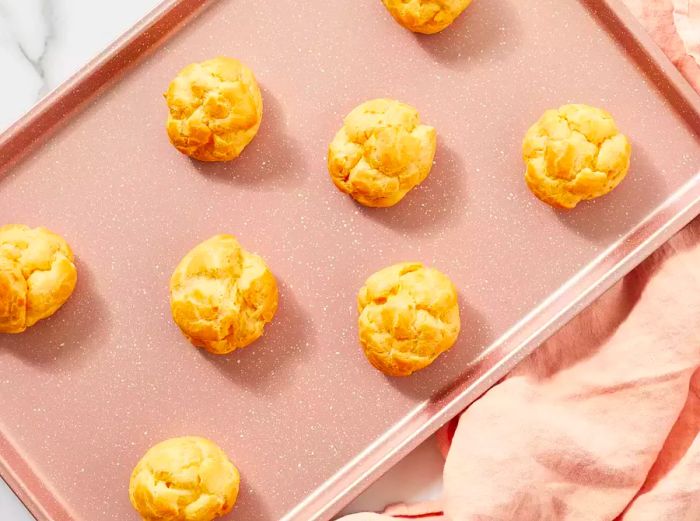 Aerial shot of freshly baked cream puffs resting on a baking sheet.