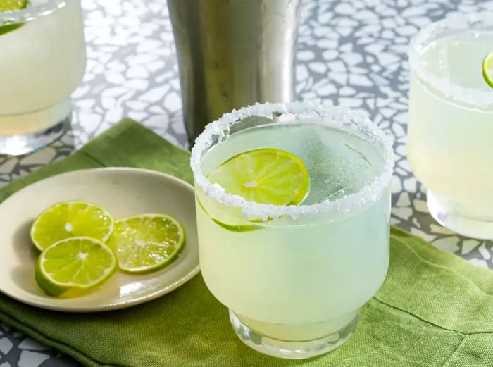 A mid-angle view of a margarita glass garnished with lime slices.