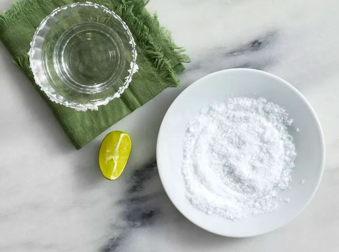 Top view of a glass with a salted rim, a plate of salt, and a lime wedge.