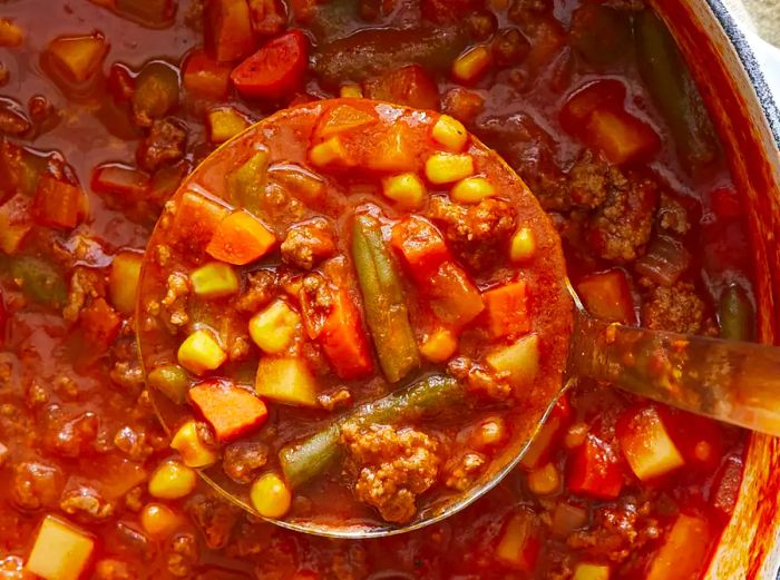 An overhead shot of a large spoonful of vegetable soup with a stock pot full beneath it