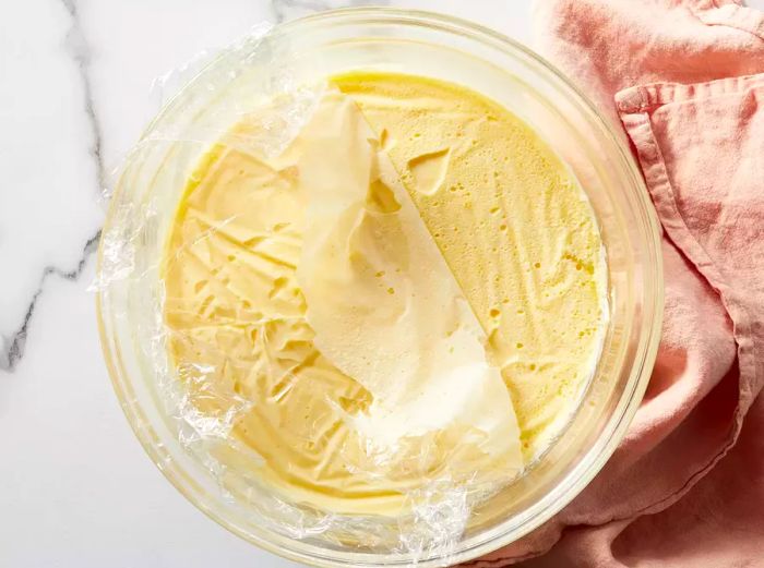 Aerial view of vanilla instant pudding in a bowl, covered with plastic wrap.