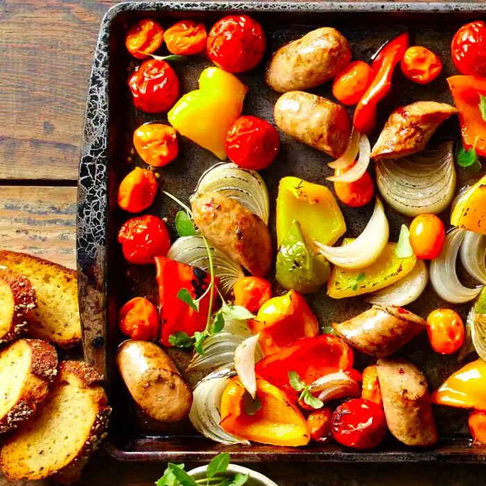 Chunks of Italian chicken sausage and colorful peppers roasted on a sheet pan, served with crusty bread on the side