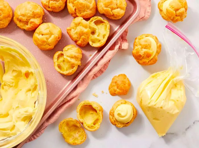 Aerial view of cream puffs being sliced in half and filled with vanilla pudding.