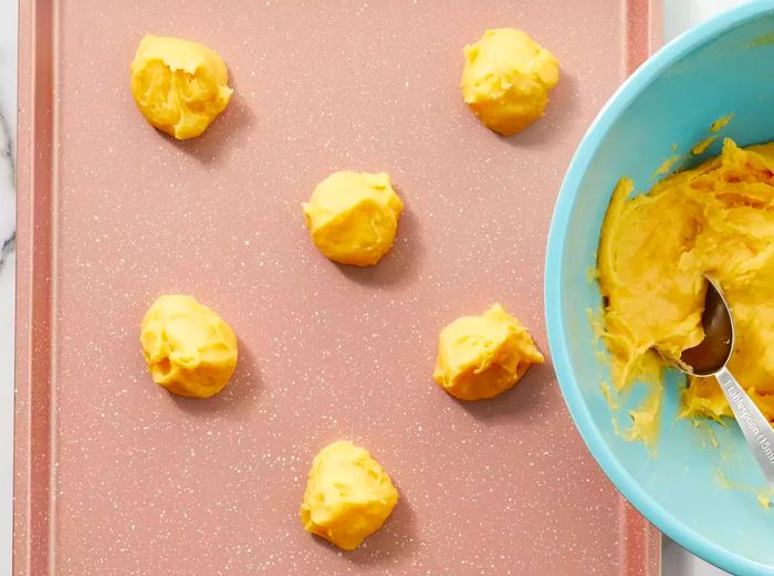 Aerial view of cream puff dough being dropped in spoonfuls onto a baking sheet.