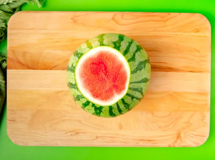 A top-down view of the watermelon on a cutting board, with both ends sliced off and one of the flat sides resting on the surface.