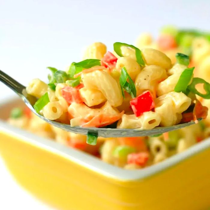 A close-up of a spoonful of macaroni salad being scooped from a square yellow bowl