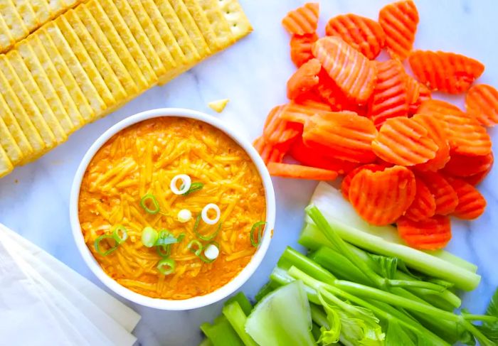 A bowl of Buffalo Chicken Dip served with crudites and chips on a platter