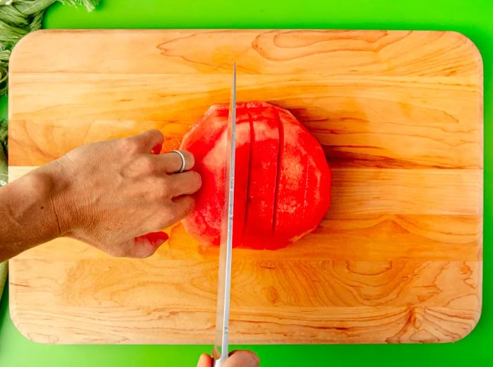 An overhead shot of hands turning the round slices of watermelon to cut them into sticks.