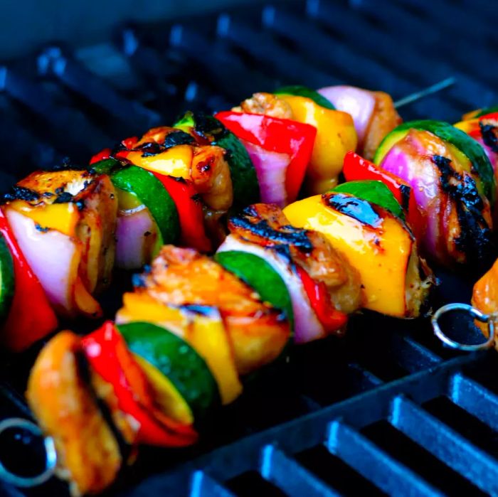 Two colorful skewers with chicken, red bell peppers, zucchini, red onion, and yellow squash sizzling on the grill