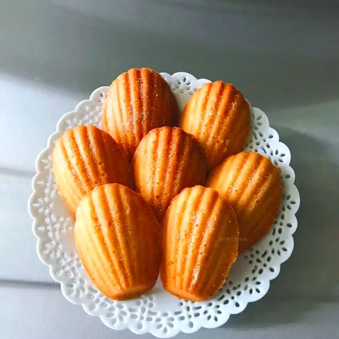 Homemade French butter cakes (Madeleines) elegantly arranged on a decorative white plate with a lace-patterned rim.