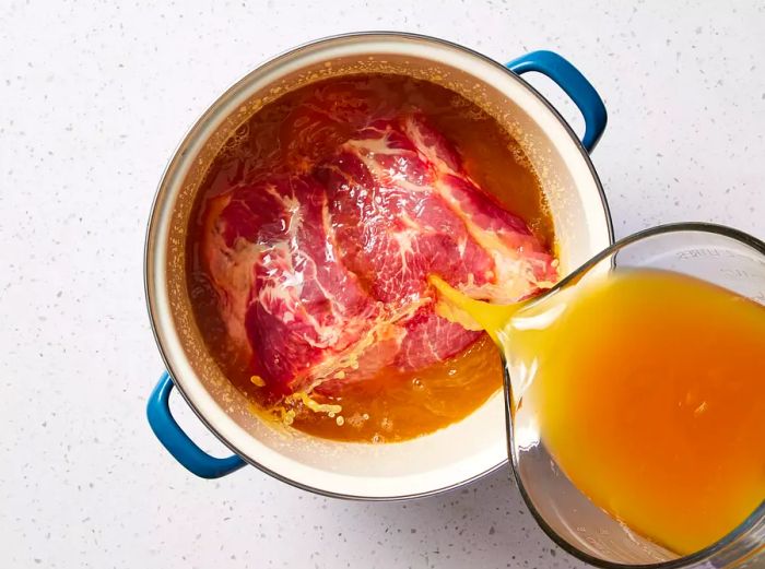 A large pot filled with apple cider vinegar being poured over a pork shoulder