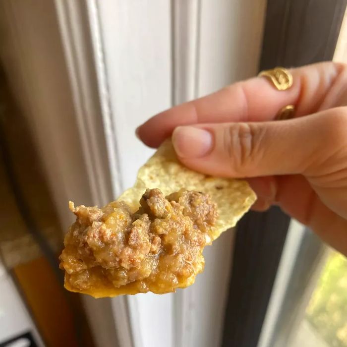 A hand holding a tortilla chip with a bit of meat sauce on top.