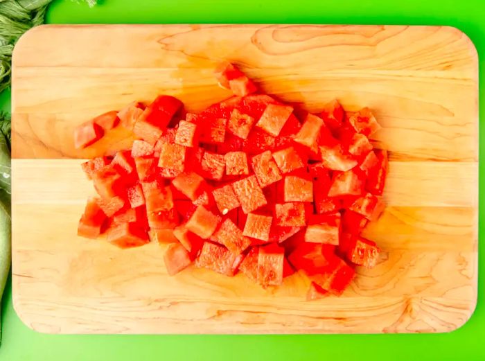 An overhead view of roughly 1-inch cubes of watermelon arranged on a cutting board.