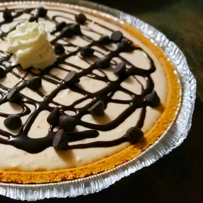 A close-up shot of a no-bake peanut butter pie, garnished with chocolate shavings and cream, all nestled in a shiny aluminum pie plate