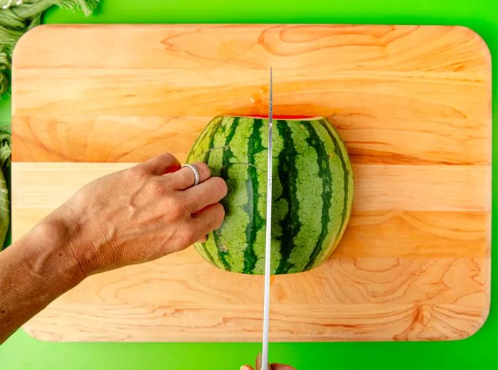 A top-down view of a watermelon being cut in half after it has already been halved once.