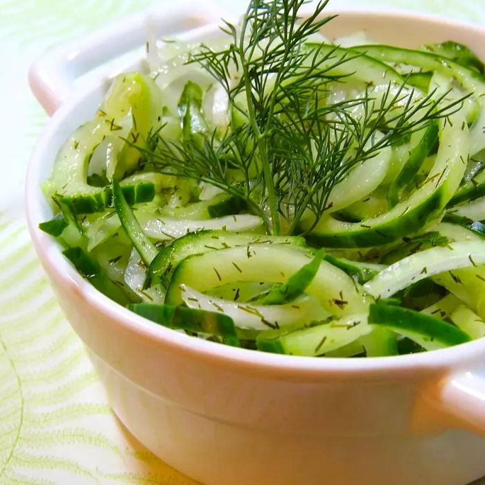 Cucumber salad in a white bowl garnished with fresh dill