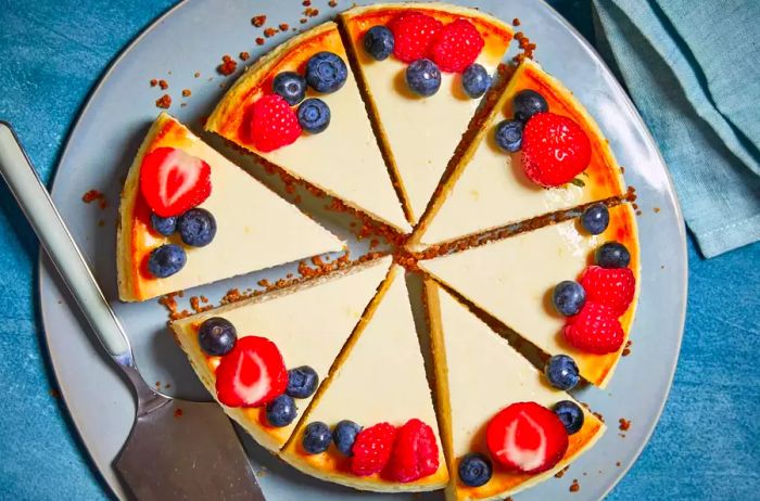 A top-down view of a cheesecake adorned with fresh strawberries, blueberries, and raspberries