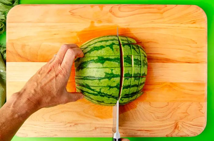 A view from above of hands cutting watermelon quarters into 1-inch cubes, creating sticks from the top down.