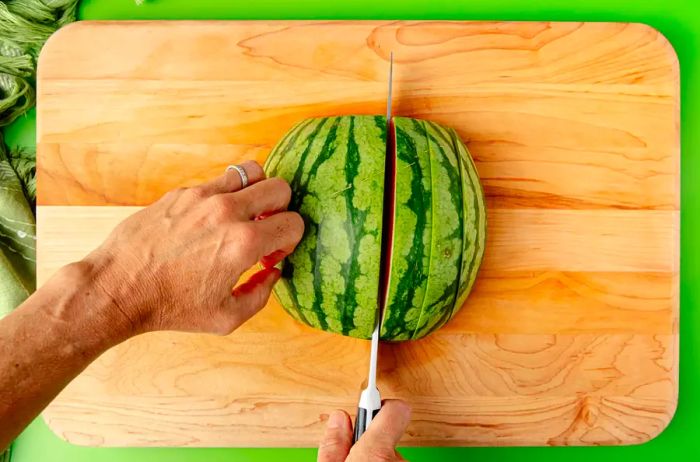 A view from above of hands cutting watermelon quarters into 1-inch wide slices.