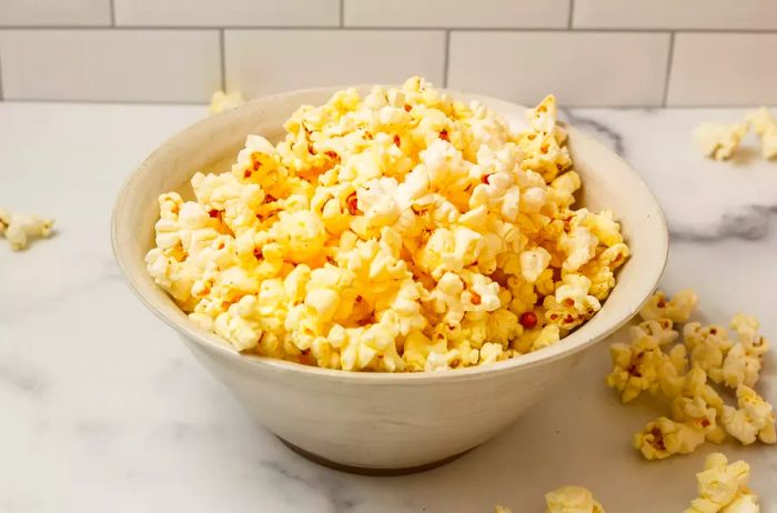 Freshly popped popcorn in a white stoneware bowl, set on a white counter with subway tiles in the background