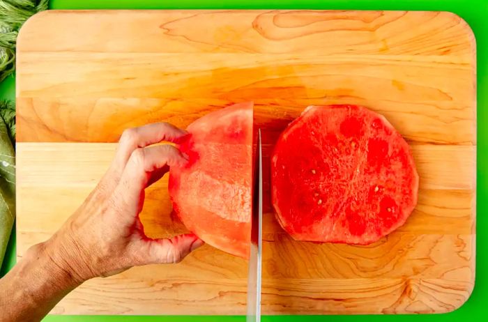 A top-down view of hands slicing a peeled watermelon into 1-inch thick rounds.