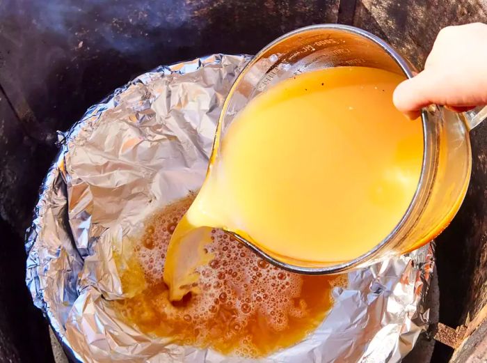 A large measuring cup filled with apple cider vinegar brine being poured into the smoker’s water pan