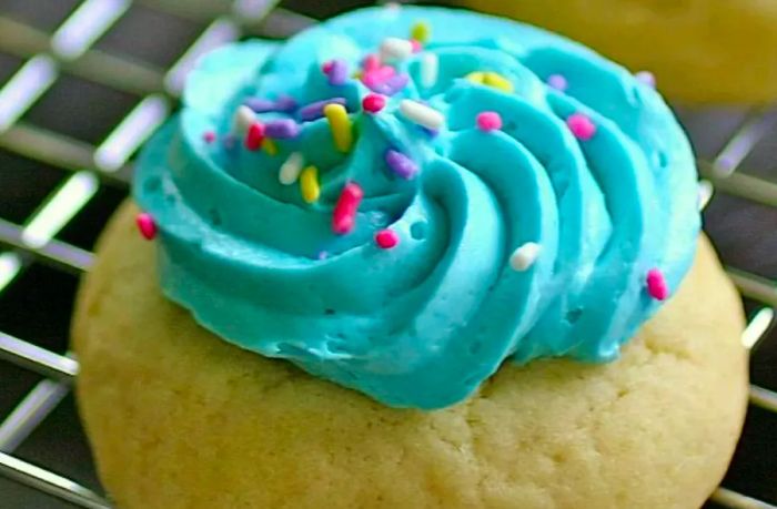 Homemade Sugar Cookie Frosting, tinted blue, swirled on top of a sugar cookie and finished with colorful candy sprinkles