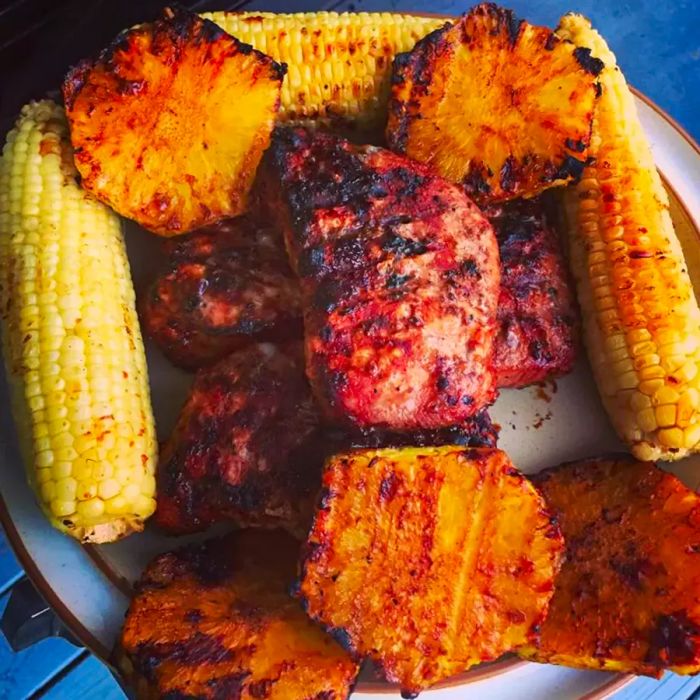 <p> A close-up shot of a platter featuring grilled Mongolian pork chops, grilled pineapple slices, and corn.</p>