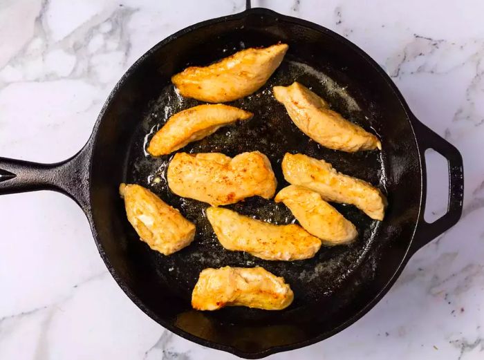 A cast iron skillet with pieces of cooked chicken breast.