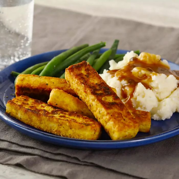 Close-up of crispy, breaded, spiced tofu served with green beans, mashed potatoes, and gravy on a blue plate.