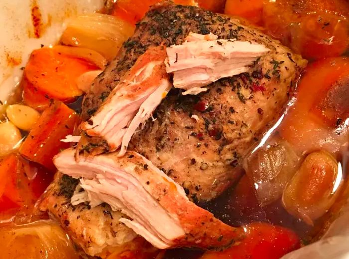 A close-up view of garlic pork roast with carrots and onions in a baking dish.