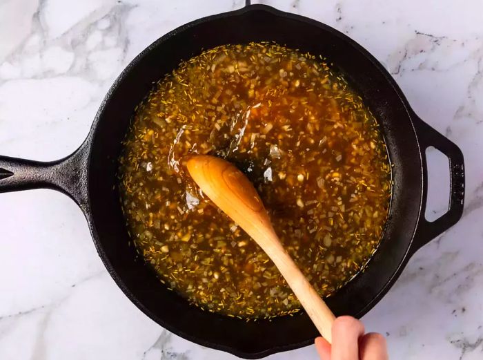 A cast iron skillet with white wine sauce being stirred with a wooden spoon.