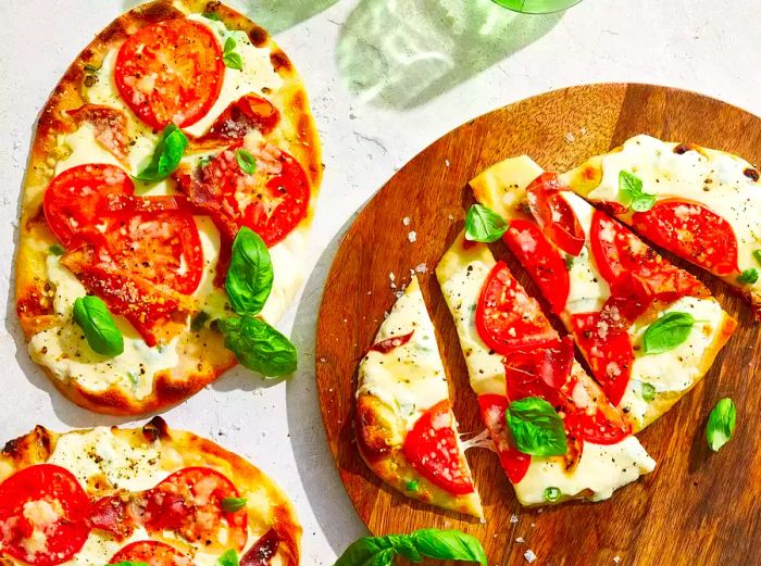 An overhead view of three naan bread Margherita pizzas with prosciutto, one sliced into four pieces.