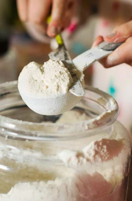 A woman carefully leveling off a measuring cup of flour