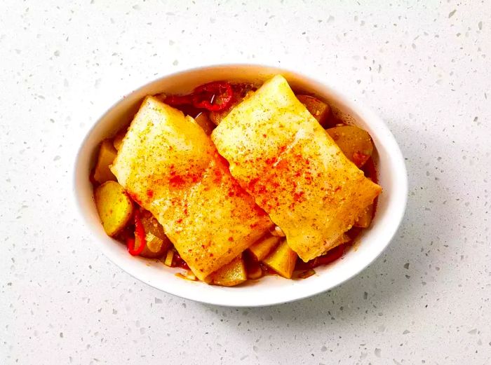 Raw Sea Bass à la Michele, topped with paprika, in a baking dish