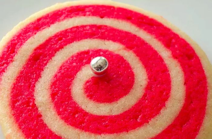 A homemade red and white Christmas Pinwheel Cookie, adorned with a shiny silver candy in the center