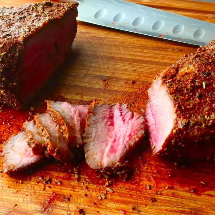 Close-up of beef tri-tip sliced on a wooden cutting board with a knife.