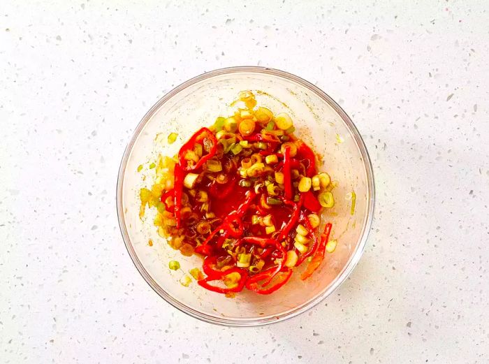 A glass bowl filled with peppers, green onions, and sauce